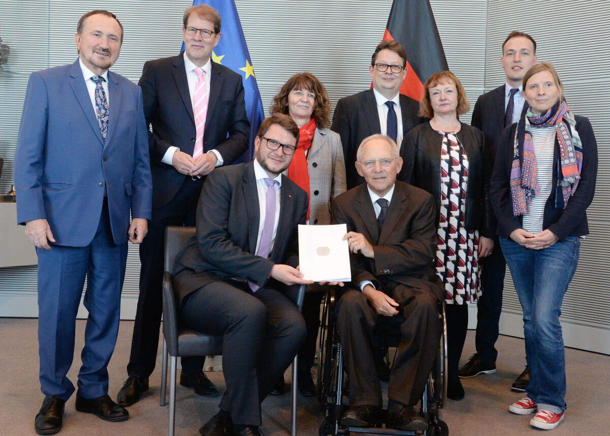 Schäuble, Wolfgang; Wendt, Marian; Todtenhausen, Manfred; Storjohann, Gero; Stamm-Fibich, Martina; Schwartze, Stefan; Kassner, Kerstin; Huber, Johannes; Rüffer, Corinna Bundestagspräsident Dr. Wolfgang Schäuble, (re), CDU/CSU, nimmt vom Vorsitzenden des Petitionsausschusses des Deutschen Bundestages, Marian Wendt, (sitzend li), CDU/CSU, im Beisein der Mitglieder des Ausschusses, (stehend v. li) Manfred Todtenhausen, FDP, Gero Storjohann, CDU/CSU, Martina Stamm-Fibich, SPD, Stefan Schwartze, SPD, Kerstin Kassner, DIE LINKE, Johannes Huber, AfD, und Corinna Rüffer, Bündnis 90/Die Grünen, den Jahresbericht 2018 entgegen.; Fahne, Fahnen, Geste, Gestik, Petition, Bericht, Präsident.