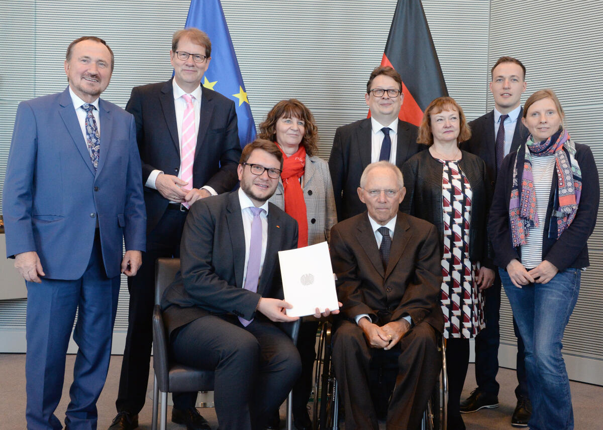 Schäuble, Wolfgang; Wendt, Marian; Todtenhausen, Manfred; Storjohann, Gero; Stamm-Fibich, Martina; Schwartze, Stefan; Kassner, Kerstin; Huber, Johannes; Rüffer, Corinna Bundestagspräsident Dr. Wolfgang Schäuble, (re), CDU/CSU, nimmt vom Vorsitzenden des Petitionsausschusses des Deutschen Bundestages, Marian Wendt, (sitzend li), CDU/CSU, im Beisein der Mitglieder des Ausschusses, (stehend v. li) Manfred Todtenhausen, FDP, Gero Storjohann, CDU/CSU, Martina Stamm-Fibich, SPD, Stefan Schwartze, SPD, Kerstin Kassner, DIE LINKE, Johannes Huber, AfD, und Corinna Rüffer, Bündnis 90/Die Grünen, den Jahresbericht 2018 entgegen.; Fahne, Fahnen, Geste, Gestik, Petition, Bericht, Präsident.