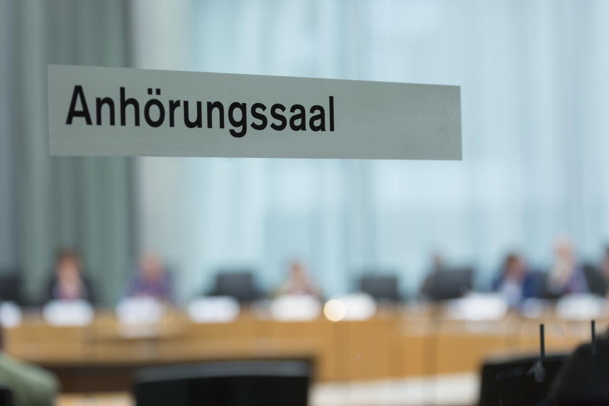  Öffentliche Sitzung des Petitionsausschusses. Blick auf die Glasstür mit der Aufschrift " Anhörungssaal".; Ausschuss, Schrift, Öffentlichkeit.
