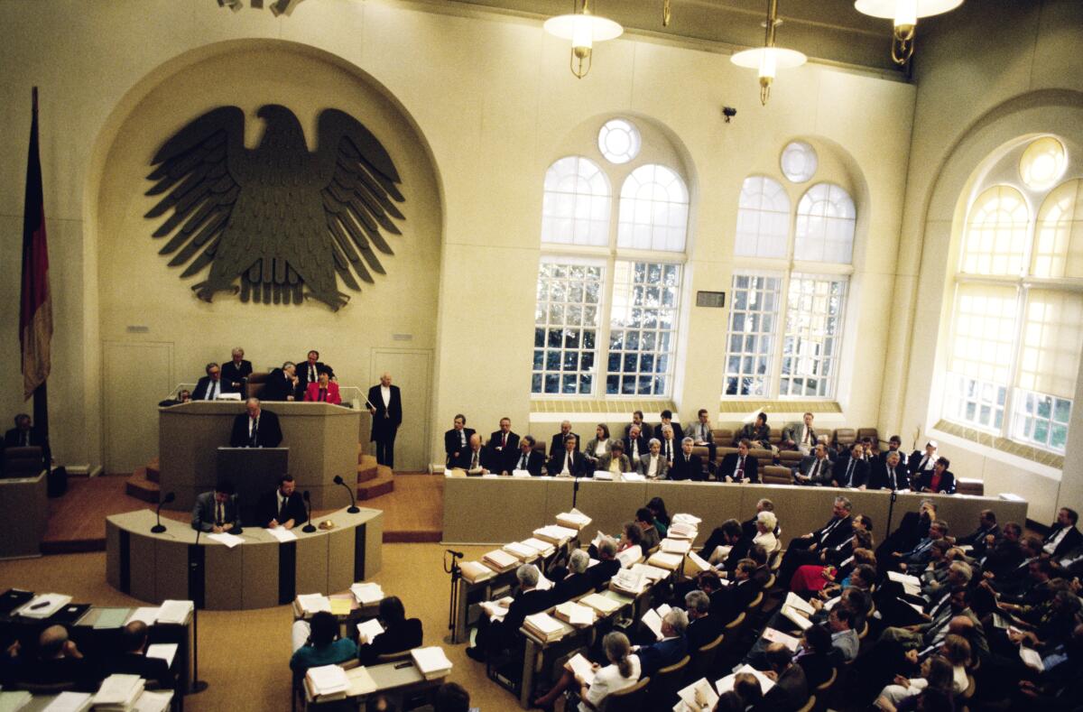 Zweite und dritte Lesung des Staatsvertrags über die "Schaffung einer Währungs-, Wirtschafts- undSozialunion zwischen der Bundesrepublik Deutschland und derDeutschen Demokratischen Republik" im Plenarsaal im Wasserwerk.; Nach mehrheitlicher Abstimmung und anschließender Verabschiedung des Gesetztes zum Einigungsvertrag, der nach der wirtschaftlichen, sozialen und Währungseinheit nun auch den Übergang zu einer staatlichen Einheit umfasst, liest Bundeskanzler Helmut Kohl, CDU/CSU, MdB, den Staatsvertrag im Plenum vor.; Lesung, Totale, Präsidium, Rednerpult, Abgeordnete, Bundestagsabgeordnete, Deutsche Einheit Kohl, Helmut Zweite und dritte Lesung des Staatsvertrags über die "Schaffung einer Währungs-, Wirtschafts- undSozialunion zwischen der Bundesrepublik Deutschland und derDeutschen Demokratischen Republik" im Plenarsaal im Wasserwerk.; Nach mehrheitlicher Abstimmung und anschließender Verabschiedung des Gesetztes zum Einigungsvertrag, der nach der wirtschaftlichen, sozialen und Währungseinheit nun auch den Übergang zu einer staatlichen Einheit umfasst, liest Bundeskanzler Helmut Kohl, CDU/CSU, MdB, den Staatsvertrag im Plenum vor.; Lesung, Totale, Präsidium, Rednerpult, Abgeordnete, Bundestagsabgeordnete, Deutsche Einheit