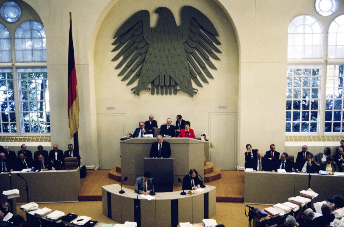 Zweite und dritte Lesung des Staatsvertrags "Schaffung einer Währungs-, Wirtschafts- undSozialunion zwischen der Bundesrepublik Deutschland und derDeutschen Demokratischen Republik" im Plenarsaal im Wasserwerk.; Nach mehrheitlicher Abstimmung und anschließender Verabschiedung des Gesetztes zum Einigungsvertrag, der nach der wirtschaftlichen, sozialen und Währungseinheit nun auch den Übergang zu einer staatlichen Einheit umfasst, liest Bundeskanzler Helmut Kohl, CDU/CSU, MdB, den Staatsvertrag im Plenum vor.; Lesung, Totale, Präsidium, Rednerpult, Abgeordnete, Bundestagsabgeordnete, Deutsche Einheit Kohl, Helmut Zweite und dritte Lesung des Staatsvertrags "Schaffung einer Währungs-, Wirtschafts- undSozialunion zwischen der Bundesrepublik Deutschland und derDeutschen Demokratischen Republik" im Plenarsaal im Wasserwerk.; Nach mehrheitlicher Abstimmung und anschließender Verabschiedung des Gesetztes zum Einigungsvertrag, der nach der wirtschaftlichen, sozialen und Währungseinheit nun auch den Übergang zu einer staatlichen Einheit umfasst, liest Bundeskanzler Helmut Kohl, CDU/CSU, MdB, den Staatsvertrag im Plenum vor.; Lesung, Totale, Präsidium, Rednerpult, Abgeordnete, Bundestagsabgeordnete, Deutsche Einheit