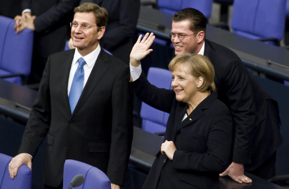 Bundeskanzlerin Dr. Angela Merkel, CDU/CSU, MdB, Bundesaußenminister Dr. Guido Westerwelle, FDP, MdB, (li.) und Bundesverteidigungsminister Dr. Freiherr Karl-Theodor zu Guttenberg, CDU/CSU, MdB, (mi.) am Tag der Wahl und Vereidigung der Bundeskanzlerin und Bundesminister.; Die Bundeskanzlerin Dr. Angela Merkel winkt jemandem zu.; Plenarsaal, Abgeordnete, Regierungsbank, Gestik Merkel, Angela; Guttenberg, Karl-Theodor Freiherr zu; Westerwelle, Guido Bundeskanzlerin Dr. Angela Merkel, CDU/CSU, MdB, Bundesaußenminister Dr. Guido Westerwelle, FDP, MdB, (li.) und Bundesverteidigungsminister Dr. Freiherr Karl-Theodor zu Guttenberg, CDU/CSU, MdB, (mi.) am Tag der Wahl und Vereidigung der Bundeskanzlerin und Bundesminister.; Die Bundeskanzlerin Dr. Angela Merkel winkt jemandem zu.; Plenarsaal, Abgeordnete, Regierungsbank, Gestik
