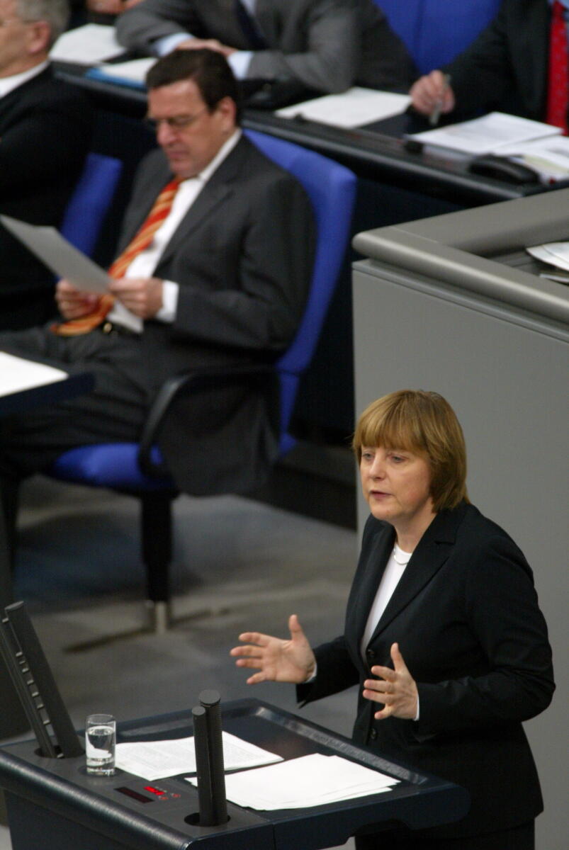 Merkel, Angela; Schröder, Gerhard Dr. Angela Merkel, CDU, Partei- und Fraktionsvorsitzende, am Rednerpult . Im Hintergrund: Gerhard Schröder, SPD, Bundeskanzler.; Abgeordnete, MdB, CDU/CSU-Fraktion, Rede, Redner, redend, Pult, Kanzler, Geste, Gestik, Deutscher Bundestag