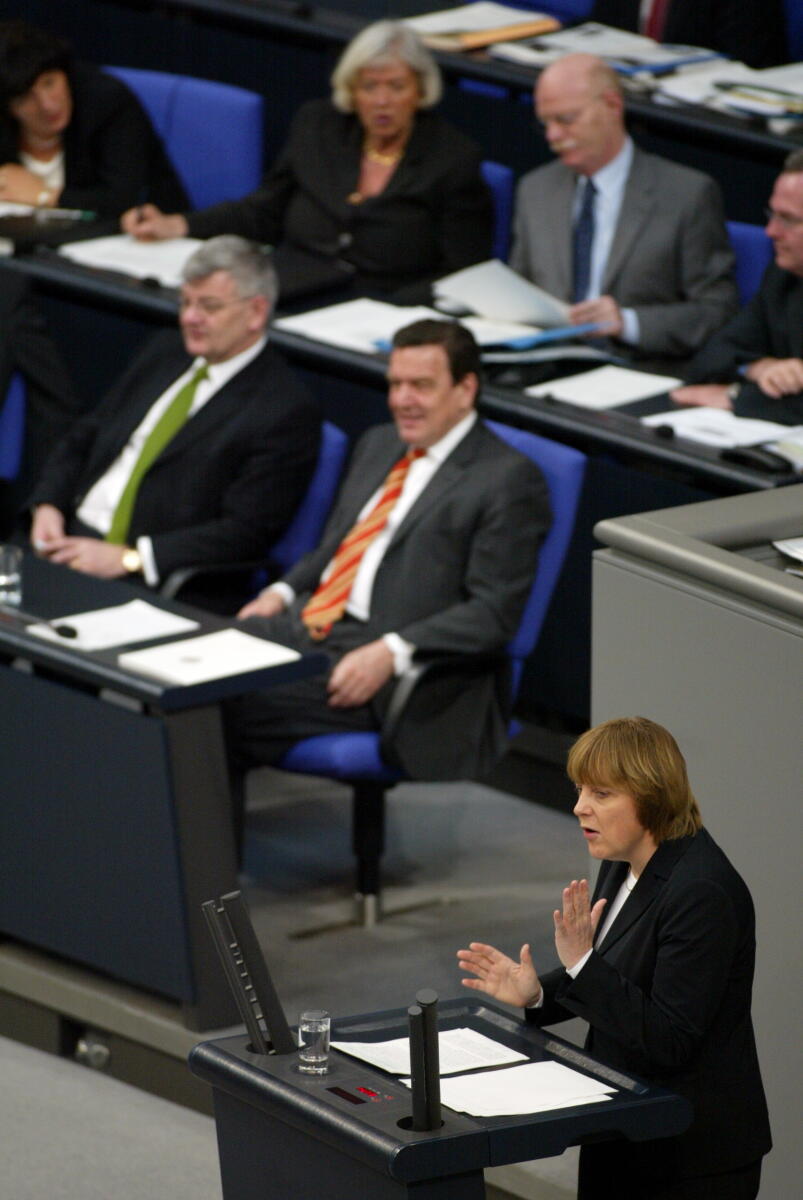 Dr. Angela Merkel, CDU, Partei- und Fraktionsvorsitzende, am Rednerpult.; Im Hindergrund: Joseph (Joschka) Fischer, Bündnis 90/Die Grünen, Bundesminister des Auswärtigen und Gerhard Schröder, SPD, Bundeskanzler; Abgeordnete, MdB, CDU/CSU-Fraktion, SPD-Fraktion, Rede, redend, Geste, Gestik Merkel, Angela; Fischer, Joseph; Schröder, Gerhard Dr. Angela Merkel, CDU, Partei- und Fraktionsvorsitzende, am Rednerpult.; Im Hindergrund: Joseph (Joschka) Fischer, Bündnis 90/Die Grünen, Bundesminister des Auswärtigen und Gerhard Schröder, SPD, Bundeskanzler; Abgeordnete, MdB, CDU/CSU-Fraktion, SPD-Fraktion, Rede, redend, Geste, Gestik