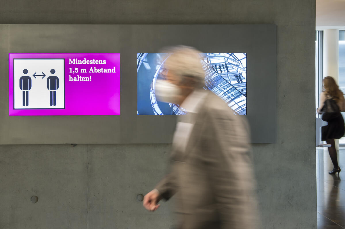 Eine Person mit Maske geht an einer elektronischen Hinweistafel zur Abstandsregel aufgrund der Covid-19-Pandemie im Paul-Löbe-Haus vorbei. Eine Person mit Maske geht an einer elektronischen Hinweistafel zur Abstandsregel aufgrund der Covid-19-Pandemie im Paul-Löbe-Haus vorbei.