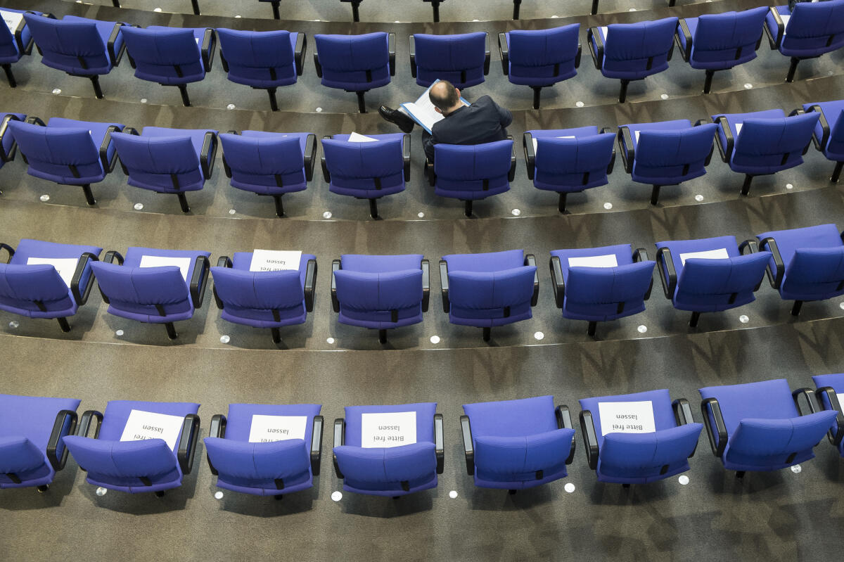 Ein Mitglied des Bundestages sitzt im Plenum neben Plätzen mit Zetteln zur Abstandsregelung aufgrund der Covid-19-Pandemie. Ein Mitglied des Bundestages sitzt im Plenum neben Plätzen mit Zetteln zur Abstandsregelung aufgrund der Covid-19-Pandemie.