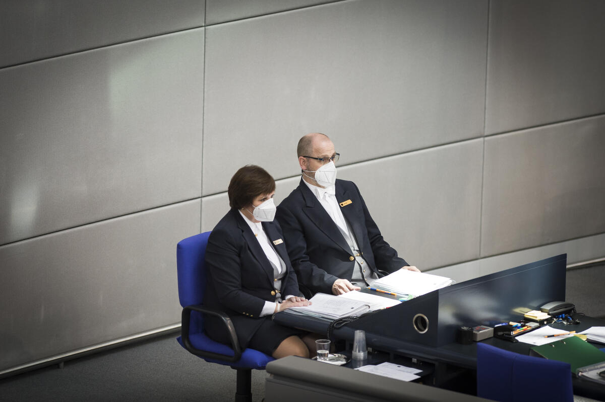 Zwei Plenarassistenten mit Maske auf ihren Plätzen beim Präsidium während der Sitzung. Zwei Plenarassistenten mit Maske auf ihren Plätzen beim Präsidium während der Sitzung.