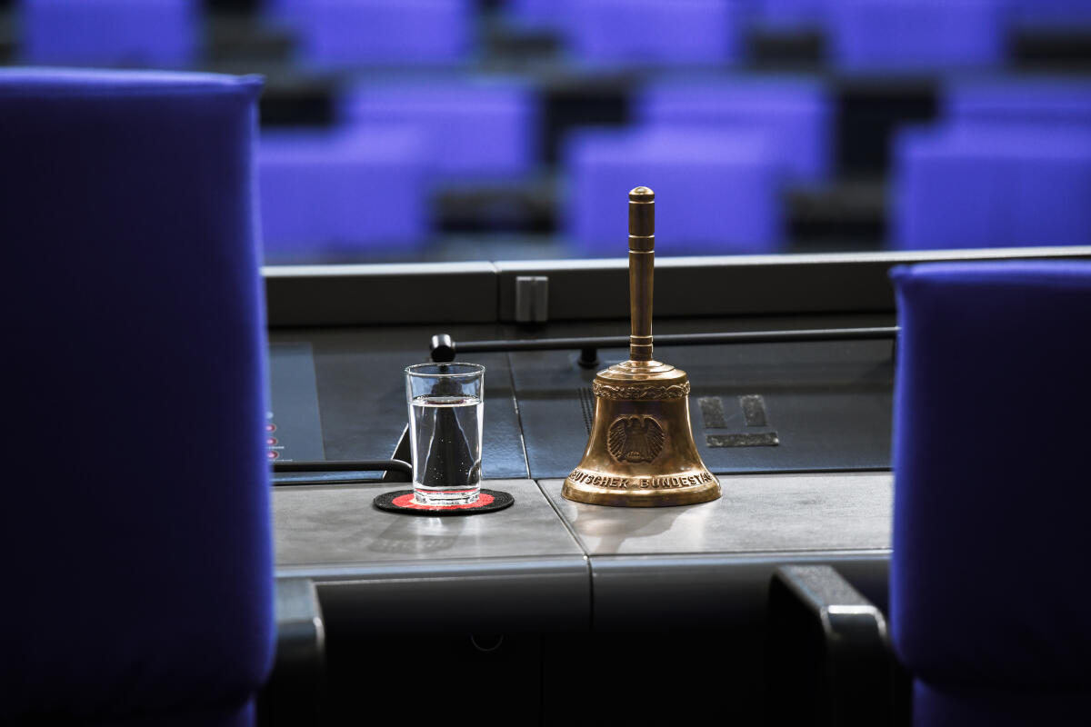 Stuhl des Bundestagspräsidenten mit einem Glass Wasser und der Glocke im Fokus. Im Hintergrund sind die Abgeordnetensitze zu sehen. Stuhl des Bundestagspräsidenten mit einem Glass Wasser und der Glocke im Fokus. Im Hintergrund sind die Abgeordnetensitze zu sehen.