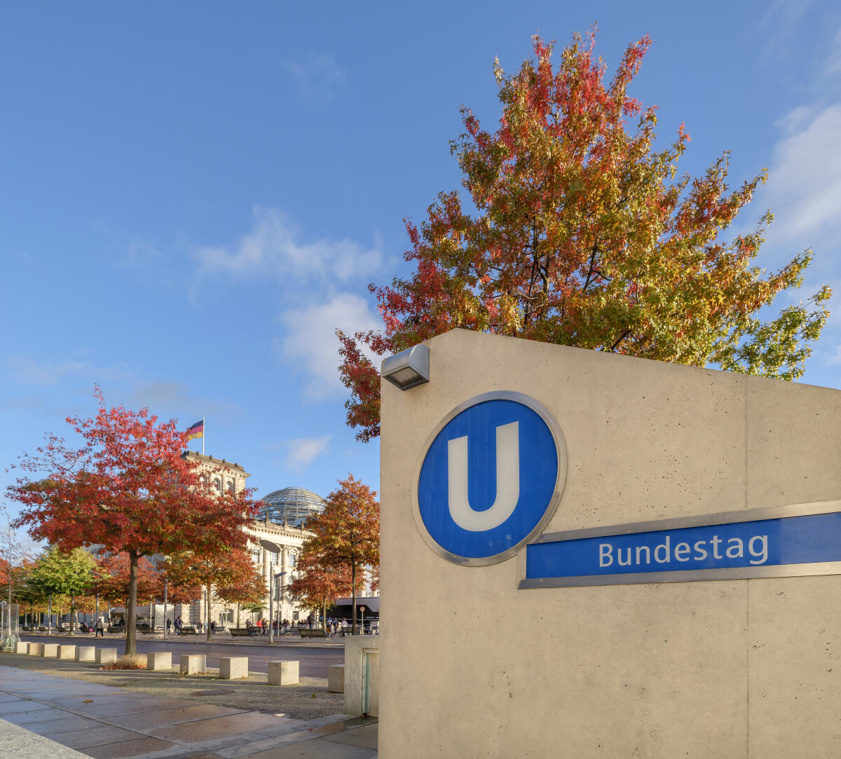 Eingang zum U-Bahnhof Bundestag mit dem Reichstagsgebäude und Bäumen mit buntem Herbstlaub im Hintergrund. Eingang zum U-Bahnhof Bundestag mit dem Reichstagsgebäude und Bäumen mit buntem Herbstlaub im Hintergrund.