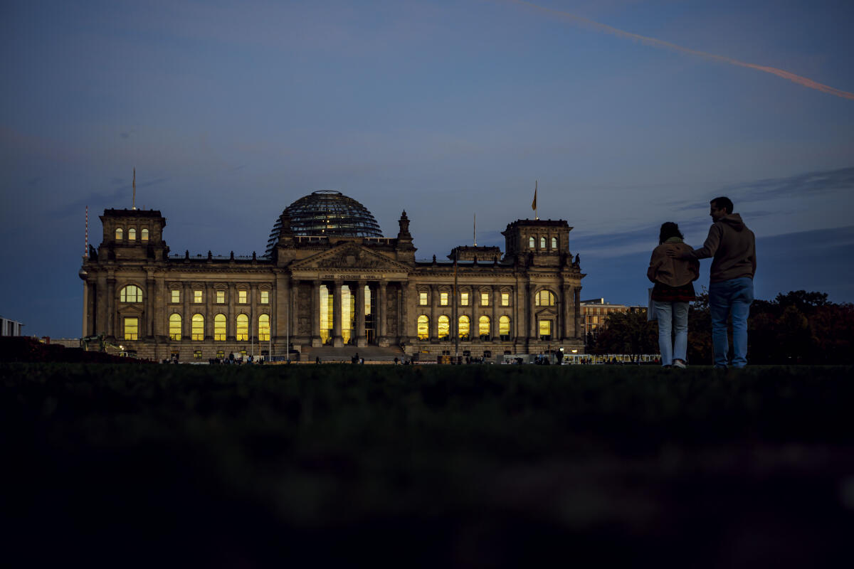 Abendstimmung am Reichstagsgebäude. In den Scheiben des Reichstages spiegelt sich der abendliche Himmel während zwei Personen im Regierungsviertel flanieren. Abendstimmung am Reichstagsgebäude. In den Scheiben des Reichstages spiegelt sich der abendliche Himmel während zwei Personen im Regierungsviertel flanieren.