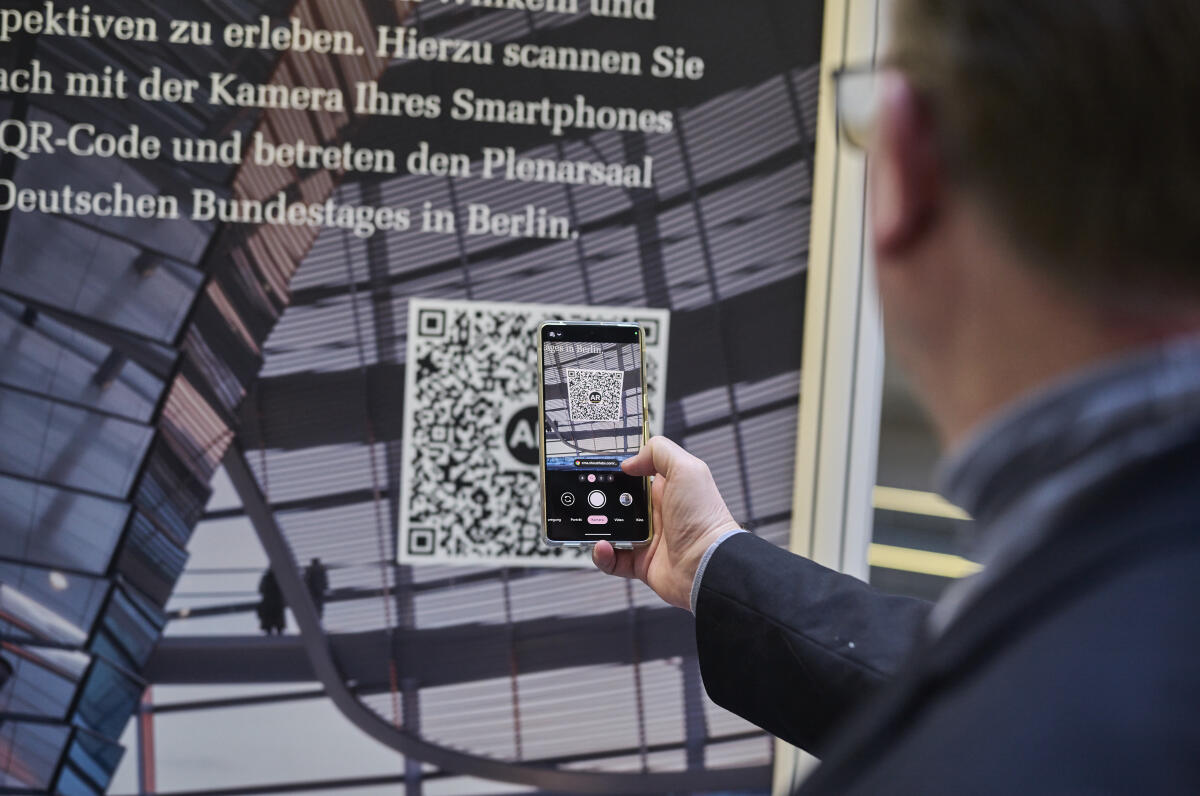  Wanderausstellung des Deutschen Bundestages in der Halle des Paul-Löbe-Hauses. Ein Besucher scannt mit einem Mobiltelefon einen QR-Code, um die Augmented Reality Funktion anzusehen, die einen virtuellen Rundgang durch den Plenarsaal des Deutschen Bundestages beinhaltet.; Die Wanderausstellung gastiert bundesweit auf Initiative von Abgeordneten und ihrer Fraktionen in einem Wahlkreis, So haben Besucherinnen und Besucher die Gelegenheit, mit ihren Wahlkreisabgeordneten ins Gespräch zu kommen.; 