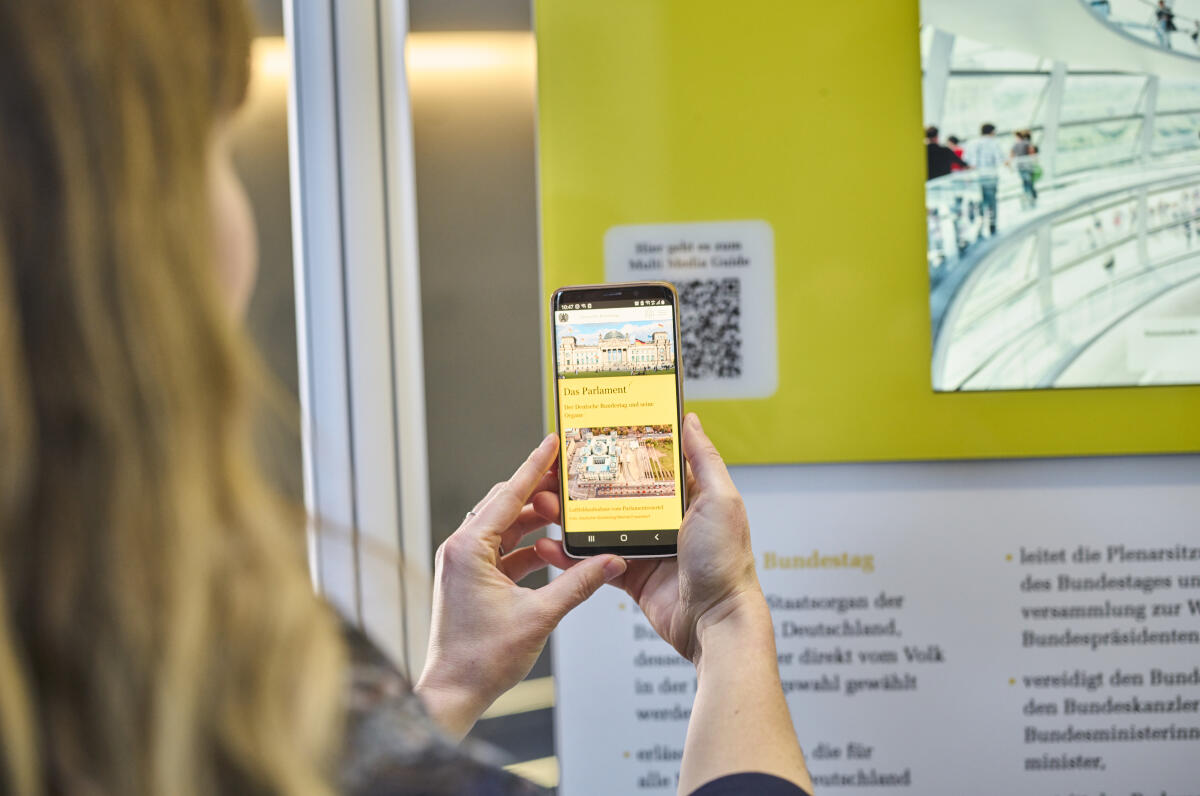 Wanderausstellung des Deutschen Bundestages in der Halle des Paul-Löbe-Hauses. Eine Besucherin scannt mit einem Mobiltelefon einen QR-Code, um sich weitere interaktive Inhalte der Ausstellung im begleitenden Multimedia-Guide anzusehen. Wanderausstellung des Deutschen Bundestages in der Halle des Paul-Löbe-Hauses. Eine Besucherin scannt mit einem Mobiltelefon einen QR-Code, um sich weitere interaktive Inhalte der Ausstellung im begleitenden Multimedia-Guide anzusehen.