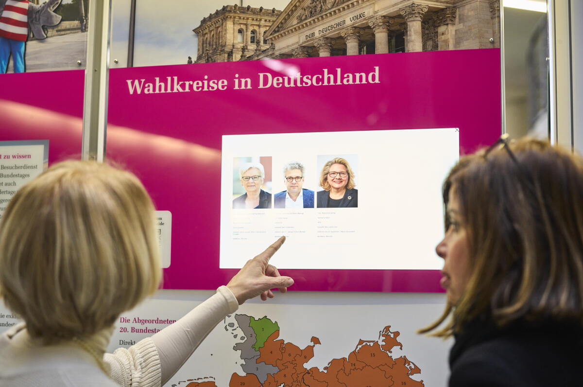  Besucherinnen sehen sich die Wanderausstellung des Deutschen Bundestages in der Halle des Paul-Löbe-Hauses an. Auf Bildschirmen und Tafeln, sowie via QR-Codes erhalten Besucher Informationen über den Deutschen Bundestag.; 