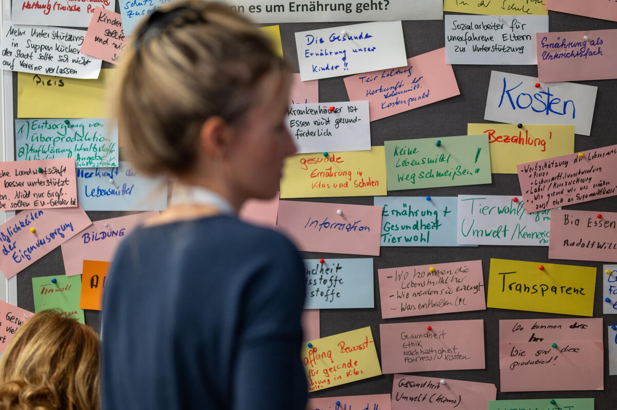 Eine Teilnehmerin des Bürgerrats, graue Pinnwand mit beschrifteten bunten Karten im Hintergrund. Eine Teilnehmerin des Bürgerrats, graue Pinnwand mit beschrifteten bunten Karten im Hintergrund.