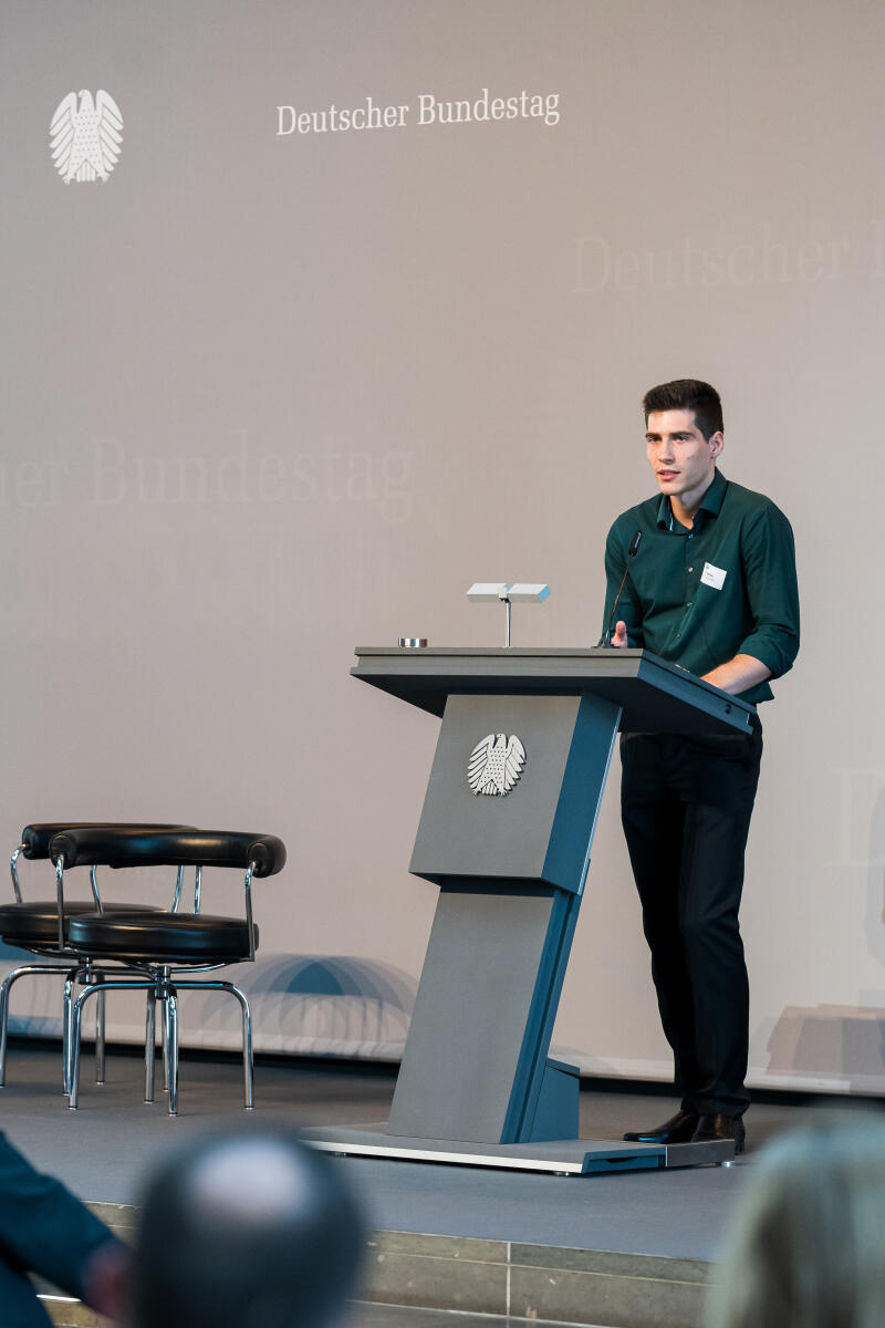 „Röhrich; Peter“ Eröffnung der Ausstellung "Poster im Bundestag: Wissenschaftsfreiheit - die Freiheit zu forschen" in der Halle des Paul-Löbe-Hauses: Peter Röhrich (im Bild), beteiligter Studierender der Technischen Hochschule Köln, beim Elevator Pitch während des Bühnenprogrammes.